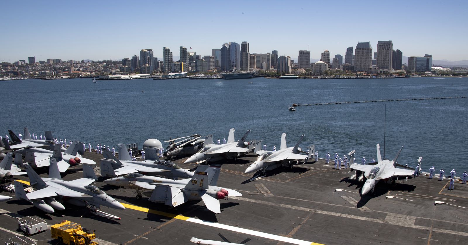 A real top gun with planes aboard an aircraft carrier and the San Diego skyline in the background.