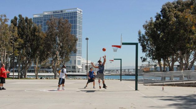 Group of guys playing basketball at the Embarcadero Marina Park South court with the Coronado Bridge in the background