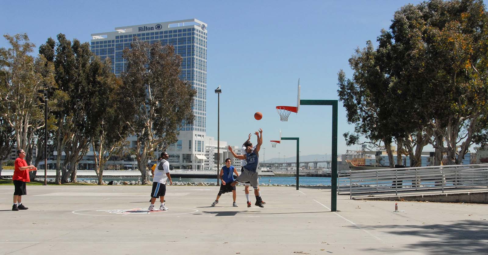Group of guys playing basketball at the Embarcadero Marina Park South court with the Coronado Bridge in the background