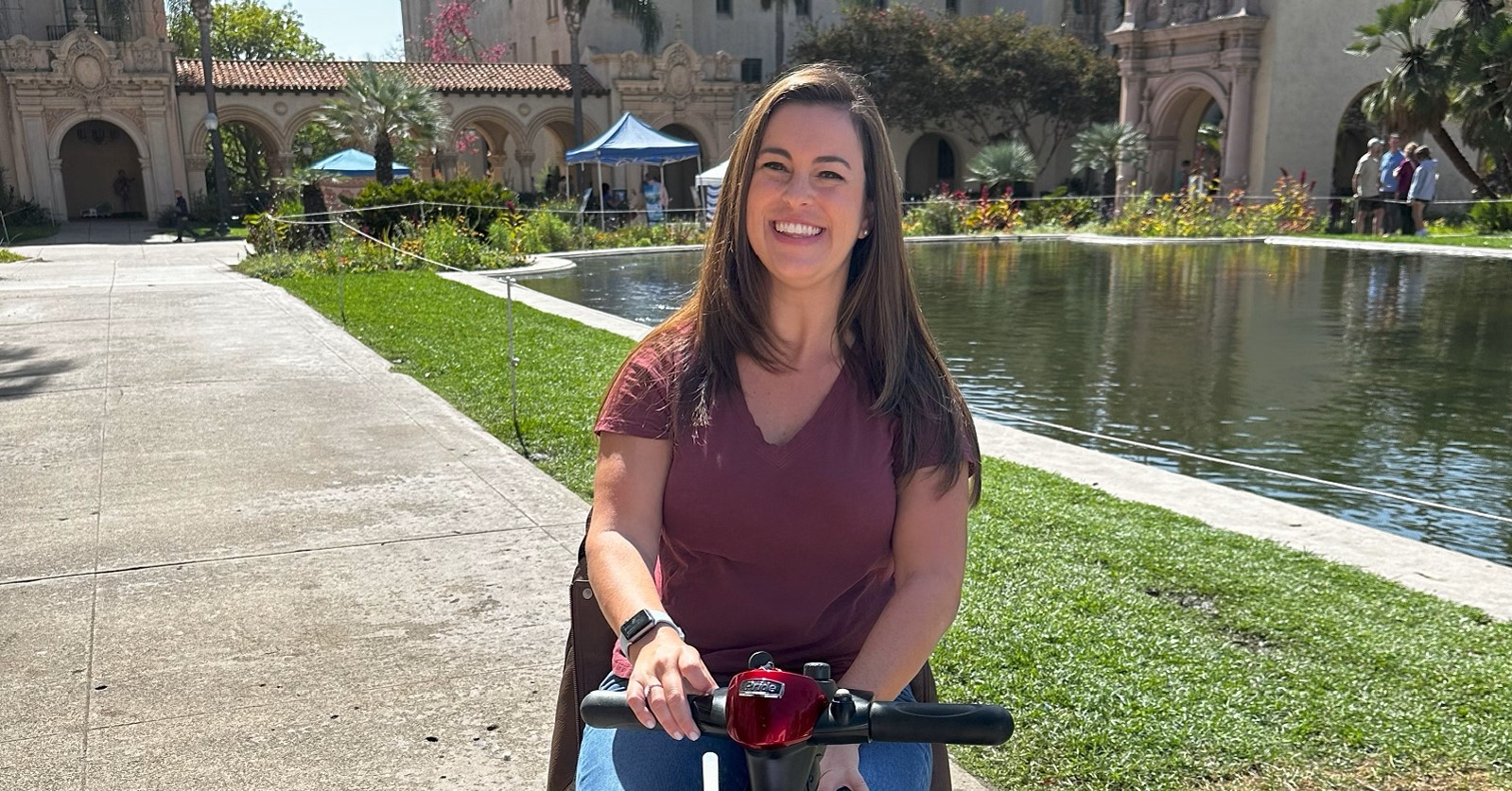 Writer Chelsea Bear sits on a mobility scooter near the Lily Pond in Balboa Park, during a tour of the park as part of her visit to San Diego.