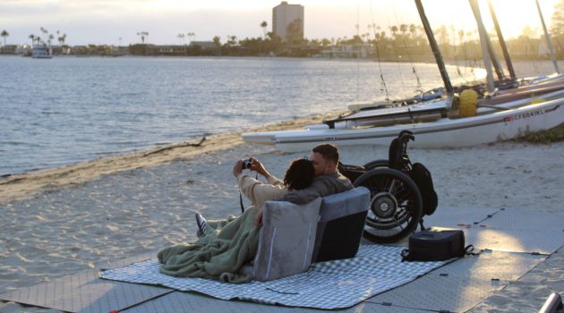 An interabled couple sits on a blanket on a beach at San Diego's Mission Bay.