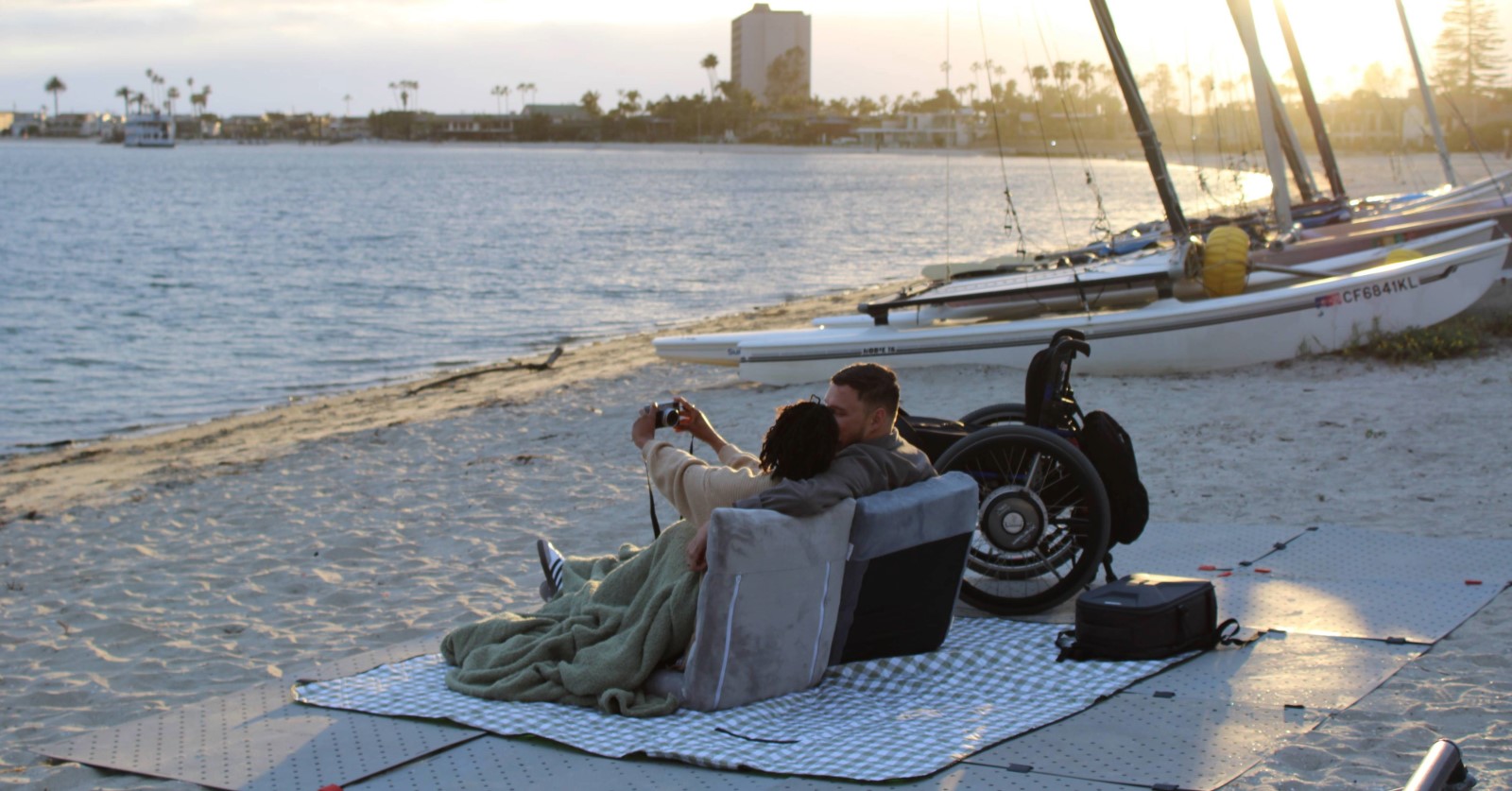 An interabled couple sits on a blanket on a beach at San Diego's Mission Bay.